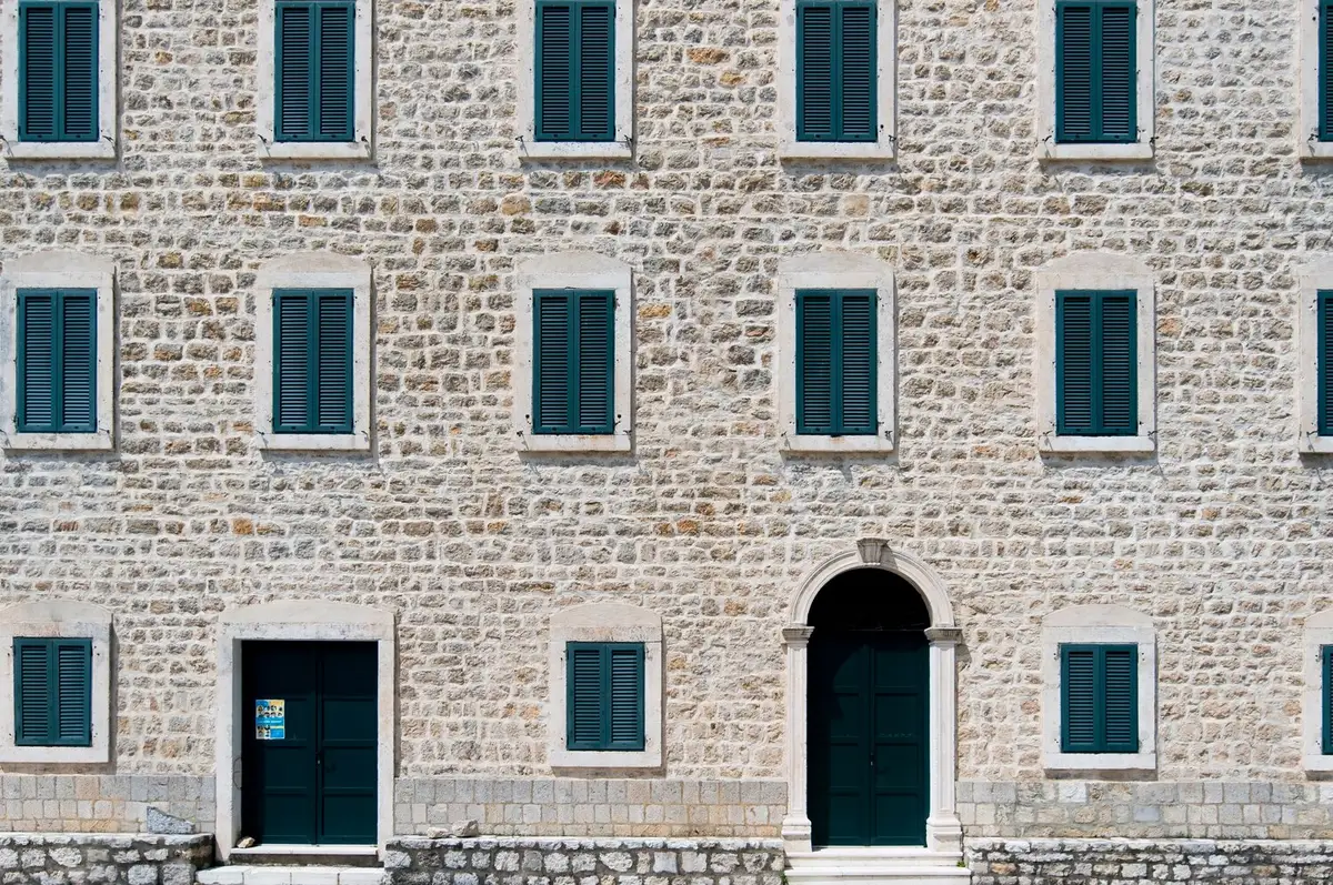 Photo d'illustration : façade en moellons de pierre calcaire avec persiennes vertes et porte cintrée