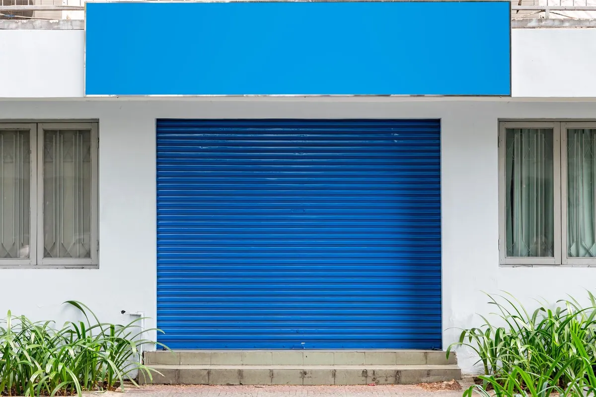 Photo d'illustration : rideau métallique bleu baissé devant un local commercial à façade blanche